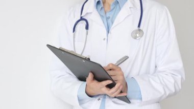 Mavi bluzun üzerine steteskop ve beyaz önlük giyen kimliği belirsiz kadın doktor tıbbi uzmanlığı ve hasta bakımını temsil eden siyah bir panoya yazı yazıyor. Tıp konsepti.