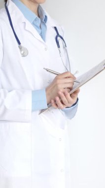 Mavi bluzun üzerine steteskop ve beyaz önlük giyen kimliği belirsiz kadın doktor tıbbi uzmanlığı ve hasta bakımını temsil eden siyah bir panoya yazı yazıyor. Tıp konsepti.