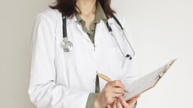 Yeşil bluz üzerine steteskop ve beyaz önlük giyen kimliği belirsiz kadın doktor tıbbi uzmanlığı ve hasta bakımını temsil eden bir panoya yazı yazıyor. İlaç ve sağlık hizmetleri kavramı.