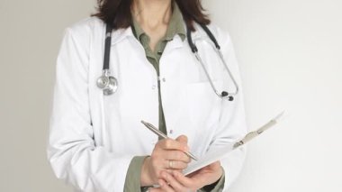 Yeşil bir bluzun üzerine steteskop ve sağlık önlüğü giyen kimliği belirsiz kadın doktor, beyaz bir panoya tıbbi uzmanlığı ve hasta bakımını temsil eden bir yazı yazıyor. Tıp konsepti.