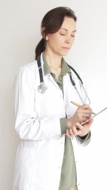 Steteskop takan doktor kadın ve yeşil bluzun üzerine beyaz önlük giymiş hasta bakımını ve tıbbi uzmanlığı temsil eden bir panoya yazı yazıyor. İlaç ve sağlık hizmetleri kavramı.