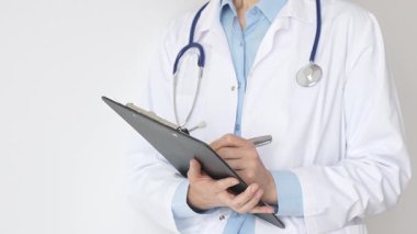 Mavi bluzun üzerine steteskop ve beyaz önlük giyen kimliği belirsiz kadın doktor tıbbi uzmanlığı ve hasta bakımını temsil eden siyah bir panoya yazı yazıyor. Tıp konsepti.