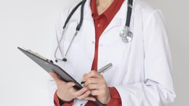 Tuğla kırmızı bluzun üzerine steteskop ve beyaz önlük giyen kimliği belirsiz kadın doktor tıbbi uzmanlığı ve hasta bakımını temsil eden bir panoya yazı yazıyor. İlaç ve sağlık hizmetleri kavramı.