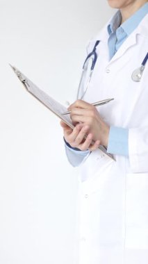 Mavi bluzun üzerine steteskop ve beyaz önlük giyen kimliği belirsiz kadın doktor tıbbi uzmanlığı ve hasta bakımını temsil eden siyah bir panoya yazı yazıyor. Tıp konsepti.