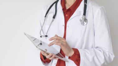 Tuğla kırmızısı bluz ve stetoskop üzerine beyaz önlük giyen kimliği belirsiz profesyonel doktor dijital tablet kullanıyor. Bu da tıpta yenilikçi sağlık uygulamaları olduğunu gösteriyor. Sağlık hizmeti kavramı