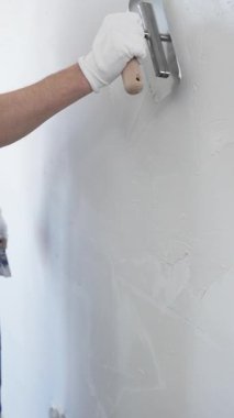 Profesyonel erkek inşaat işçisi, ev yenileme ve iç dekorasyon konusunda uzmanlığını göstermek için duvara alçı yapıştırmak için son bir mala kullanıyor. Dikey görünüm.