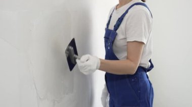 Profesyonel kadın inşaat işçisi, duvarlara alçı yapıştırmak için son malayı kullanıyor. Bu da ev yenileme ve iç dekorasyon konusunda uzman olduğunu gösteriyor..