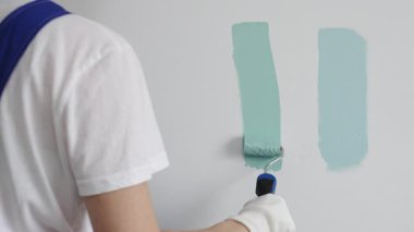 Boya rulosu kullanan bir ressam, açık yeşil rengin iki tonunu karşılaştırıyor, bir ev yenileme projesi sırasında duvar rengi için dikkatli bir seçim yapıyor. İç tasarım için mükemmel bir renk seçiliyor