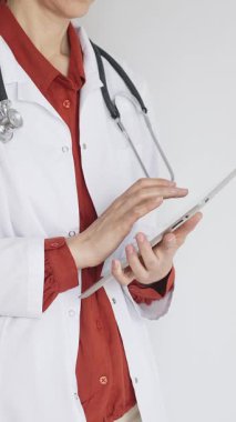 Tuğla kırmızısı bluz ve stetoskop üzerine beyaz önlük giyen kimliği belirsiz profesyonel doktor dijital tablet kullanıyor. Bu da tıpta yenilikçi sağlık uygulamaları olduğunu gösteriyor. Sağlık hizmeti kavramı