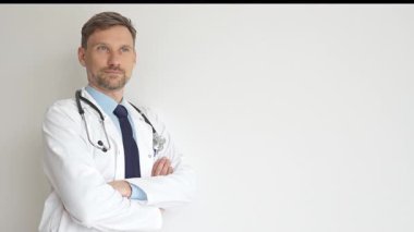 Kendine güvenen erkek doktor kolları çapraz duruyor, steteskop ve beyaz önlük giyiyor. Düşünceli bir şekilde, tıp alanında profesyonelliği ve uzmanlığı somutlaştırıyor. İlaç ve sağlık hizmetleri