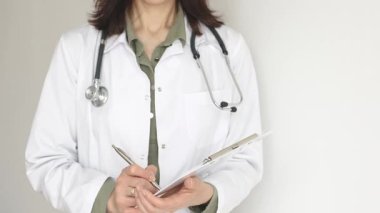 Yeşil bir bluzun üzerine steteskop ve sağlık önlüğü giyen kimliği belirsiz kadın doktor, beyaz bir panoya tıbbi uzmanlığı ve hasta bakımını temsil eden bir yazı yazıyor. Tıp konsepti.