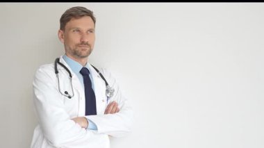 Kendine güvenen erkek doktor kolları çapraz duruyor, steteskop ve beyaz önlük giyiyor. Düşünceli bir şekilde, tıp alanında profesyonelliği ve uzmanlığı somutlaştırıyor. İlaç ve sağlık hizmetleri