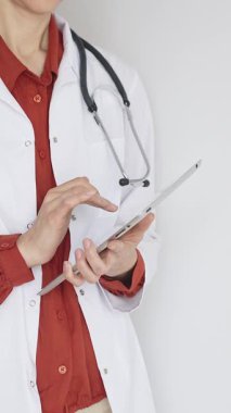 Tuğla kırmızısı bluz ve stetoskop üzerine beyaz önlük giyen kimliği belirsiz profesyonel doktor dijital tablet kullanıyor. Bu da tıpta yenilikçi sağlık uygulamaları olduğunu gösteriyor. Sağlık hizmeti kavramı