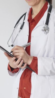 Tuğla kırmızı bluzun üzerine steteskop ve beyaz önlük giyen kimliği belirsiz kadın doktor tıbbi uzmanlığı ve hasta bakımını temsil eden bir panoya yazı yazıyor. İlaç ve sağlık hizmetleri kavramı.