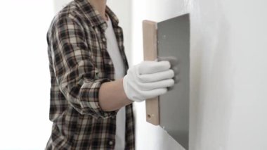 Meçhul kadın inşaat işçisi giyiniyor ve kareli gömlek profesyonel kalitede spatulayla sıva sürüyor. Ev yenileme projesi sırasında ustalıkla yapılmış beyaz duvarı düzleştiriyor..