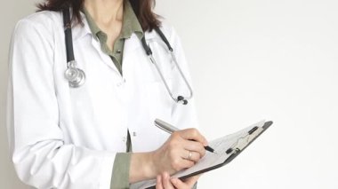 Yeşil bluz üzerine steteskop ve beyaz önlük giyen kimliği belirsiz kadın doktor tıbbi uzmanlığı ve hasta bakımını temsil eden bir panoya yazı yazıyor. İlaç ve sağlık hizmetleri kavramı.
