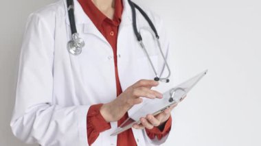 Tuğla kırmızısı bluz ve stetoskop üzerine beyaz önlük giyen kimliği belirsiz profesyonel doktor dijital tablet kullanıyor. Bu da tıpta yenilikçi sağlık uygulamaları olduğunu gösteriyor. Sağlık hizmeti kavramı