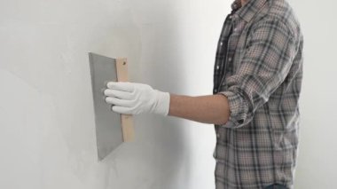 Bilinmeyen erkek inşaat işçisi koruyucu eldivenler ve ekose gömlek giyiyor. Tadilat projesi sırasında profesyonel alçıpan bantlama bıçağını kullanarak duvarın yüzeyine sorunsuzca alçı yayıyor..