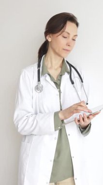 Yeşil bluz ve steteskop üzerine laboratuvar önlüğü giyen kendine güvenen doktor kadın doktor modern sağlık ve tıbbi teknolojiyi temsil eden dijital tablet kullanıyor. Tıp konsepti.