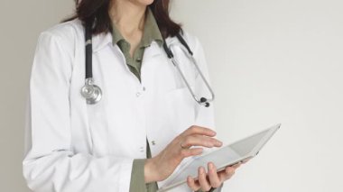 Yeşil bluz ve steteskop üzerine beyaz önlük giyen kimliği belirsiz kadın doktor dijital tablet kullanıyor. Bu da tıpta yenilikçi sağlık uygulamaları olduğunu gösteriyor. Sağlık hizmeti kavramı.