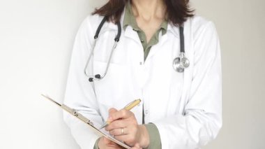 Stetoskop ve yeşil bluzun üzerine beyaz önlük giyen kimliği belirsiz bir kadın doktor tahta renkli bir panoya tıbbi uzmanlığı ve hasta bakımını temsil eden bir yazı yazıyor. Tıp konsepti