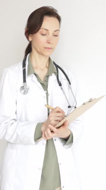 Steteskop takan doktor kadın ve yeşil bluzun üzerine beyaz önlük giymiş hasta bakımını ve tıbbi uzmanlığı temsil eden bir panoya yazı yazıyor. İlaç ve sağlık hizmetleri kavramı.