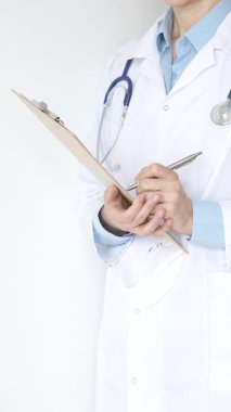 Mavi bluzun üzerine steteskop ve beyaz önlük giyen kimliği belirsiz kadın doktor tıbbi uzmanlığı ve hasta bakımını temsil eden siyah bir panoya yazı yazıyor. Tıp konsepti.