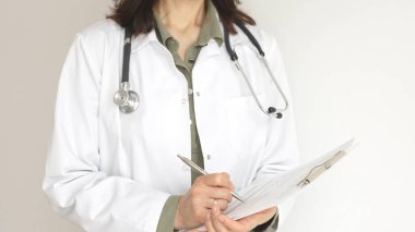 Yeşil bir bluzun üzerine steteskop ve sağlık önlüğü giyen kimliği belirsiz kadın doktor, beyaz bir panoya tıbbi uzmanlığı ve hasta bakımını temsil eden bir yazı yazıyor. Tıp konsepti.
