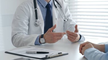 Erkek doktor teşhisi açıklıyor, klinik ortamdaki muayeneler sırasında hastaya el kol hareketi yapıyor. Tıp ve sağlık hizmetleri kavramı.