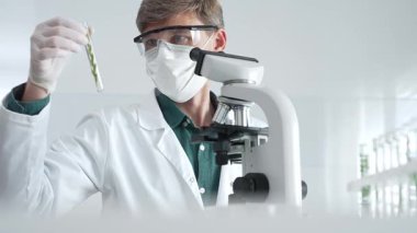 Biyolojik analiz sırasında steril bir laboratuvarda yeşil botanik örneklerini inceleyen maskeli yetişkin bir araştırmacı. Tıp, sağlık ve bilim konsepti.