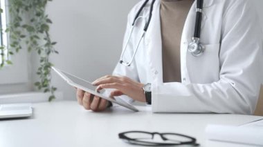 Tablet üzerindeki hasta verilerini inceleyen, çağdaş klinik ortamlarda beyaz laboratuvar önlüğü ve steteskop giyen, dijital sağlık danışmanlığı yapan bir tıp uzmanı. İlaç ve sağlık hizmetleri