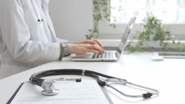 Stetoskop ve tıbbi kayıtlar doktorun karşısındaki masada. Bilgisayarında tıbbi bir büro var. İnternet üzerinden sağlık hizmeti ya da teletıp hizmeti sunuyor. Tıp konsepti.