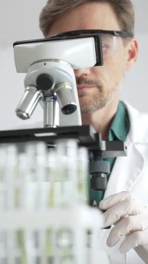 Koruyucu ekipman araştırmacısı steril bir laboratuvar ortamında mikroskopla numuneleri analiz ediyor. Tıp, sağlık ve bilim konsepti.