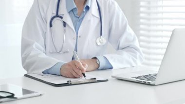 Tıbbi pratisyen, etrafını laptoplar, tabletler ve gözlüklerle donatarak hasta bakımı için odaklanmış bir atmosfer yaratıyor.