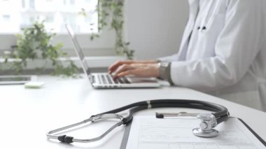 Stetoskop ve tıbbi kayıtlar doktorun karşısındaki masada. Bilgisayarında tıbbi bir büro var. İnternet üzerinden sağlık hizmeti ya da teletıp hizmeti sunuyor. Tıp konsepti.