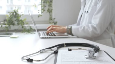 Tıbbi kayıtlar üzerinde steteskop var. Doktorun bilgisayarında yazdığı bilgisayarın karşısında duruyor. Bu da sağlık hizmeti ya da teletıp hizmetlerini gösteriyor. Tıp konsepti.