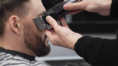 Profesyonel berber, müşterinin sakalını elektrikli jiletle dikkatlice buduyor. Modern bir berber dükkanında kusursuz ve şık bir tımar deneyimi sunuyor.