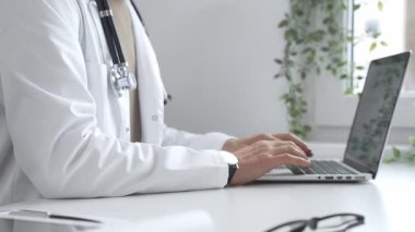 Laptop üzerinde çalışan, modern, iyi aydınlatılmış sağlık ortamında beyaz önlük ve steteskop giyen, klinik uzmanlığı dijital teknolojiyle harmanlayan bir tıp uzmanı. İlaç ve sağlık hizmetleri