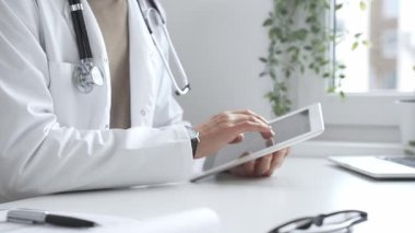 Tablet üzerindeki hasta verilerini inceleyen, çağdaş klinik ortamlarda beyaz laboratuvar önlüğü ve steteskop giyen, dijital sağlık danışmanlığı yapan bir tıp uzmanı. İlaç ve sağlık hizmetleri