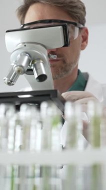 Koruyucu ekipman araştırmacısı steril bir laboratuvar ortamında mikroskopla numuneleri analiz ediyor. Tıp, sağlık ve bilim konsepti.