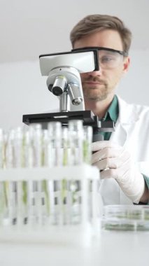 Beyaz koruyucu giysiler içinde erkek bilim araştırmacısı steril bir laboratuvar ortamında mikroskopla numuneleri analiz ediyor. Tıp, sağlık ve bilim konsepti.