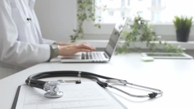 Stetoskop ve tıbbi kayıtlar doktorun karşısındaki masada. Bilgisayarında tıbbi bir büro var. İnternet üzerinden sağlık hizmeti ya da teletıp hizmeti sunuyor. Tıp konsepti.