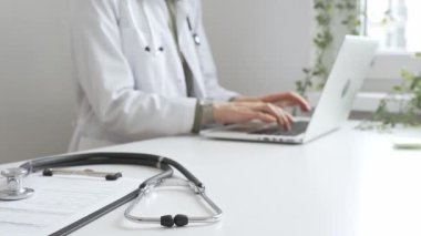 Stetoskop ve tıbbi kayıtlar doktorun karşısındaki masada. Bilgisayarında tıbbi bir büro var. İnternet üzerinden sağlık hizmeti ya da teletıp hizmeti sunuyor. Tıp konsepti.