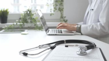 Stetoskop ve tıbbi kayıtlar doktorun karşısındaki masada. Bilgisayarında tıbbi bir büro var. İnternet üzerinden sağlık hizmeti ya da teletıp hizmeti sunuyor. Tıp konsepti.