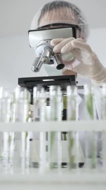 Mikroskop kullanarak beyaz koruyucu kıyafet giyen kadın bilim adamı laboratuarda test tüplerini analiz ediyor, bilimsel araştırma ve geliştirme yapıyor. Tıp, sağlık ve bilim konsepti.