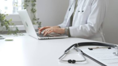 Stetoskop ve tıbbi kayıtlar doktorun karşısındaki masada. Bilgisayarında tıbbi bir büro var. İnternet üzerinden sağlık hizmeti ya da teletıp hizmeti sunuyor. Tıp konsepti.