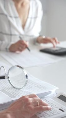 Hesap makinesi kullanan ve notlar alan bir muhasebecinin muhasebe, finans ve vergi hazırlıklarını vurguladığı mali belgelerde büyüteç kapat. Ticarette denetim ve vergiler.