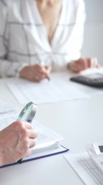 Profesyonel muhasebeciler, parlak ofislerindeki mali raporları denetlemek için bir büyüteç ve hesap makinesi kullanarak birlikte çalışıyorlar. Denetim ve vergi kavramı.