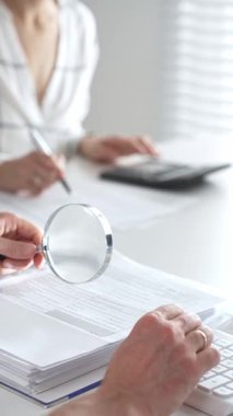 Hesap makinesi kullanan ve notlar alan bir muhasebecinin muhasebe, finans ve vergi hazırlıklarını vurguladığı mali belgelerde büyüteç kapat. Ticarette denetim ve vergiler.