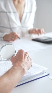 Profesyonel muhasebeciler, parlak ofislerindeki mali raporları denetlemek için bir büyüteç ve hesap makinesi kullanarak birlikte çalışıyorlar. Denetim ve vergi kavramı.